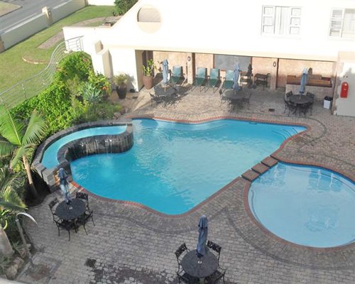 An outdoor pool and hot tub with patio and chaise lounge chairs.