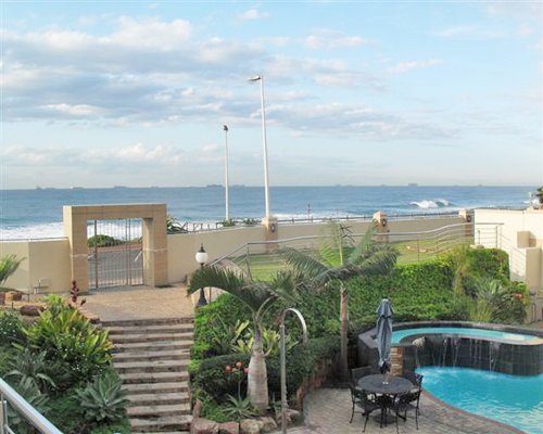 Outdoor swimming pool with patio chairs and ocean view.