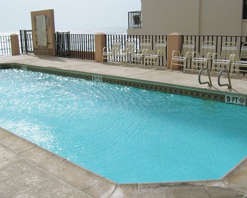 An outdoor swimming pool with patio chairs alongside ocean.
