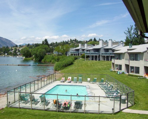 AN OUTDOOR SWIMMING POOL WITH CHAISE LOUNGE CHAIRS ALONGSIDE RESORT AND THE LAKE.