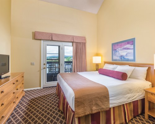 A WELL FURNISHED BEDROOM WITH A TELEVISION AND BALCONY.