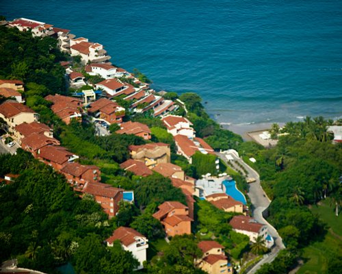 An aerial view of buildings surrounded by wooded area alongside the ocean.