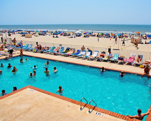 Outdoor swimming pool with chaise lounge chairs and sunshades alongside the beach.