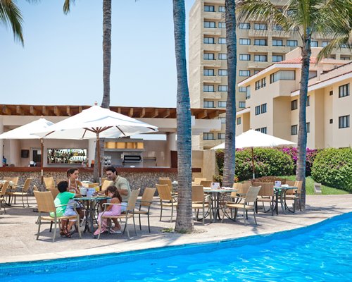 An outdoor dining area with coconut trees alongside a pool and the resort.