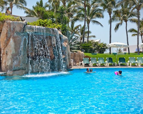 Outdoor grotto pool with chaise lounge chairs sunshades and palm trees.