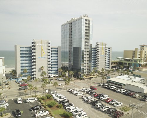 Exterior view of resort with multiple balconies parking lot and palm trees.