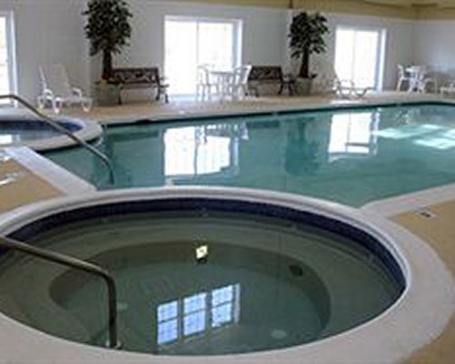 An indoor hot tub with swimming pool alongside chaise lounge chairs and patio.