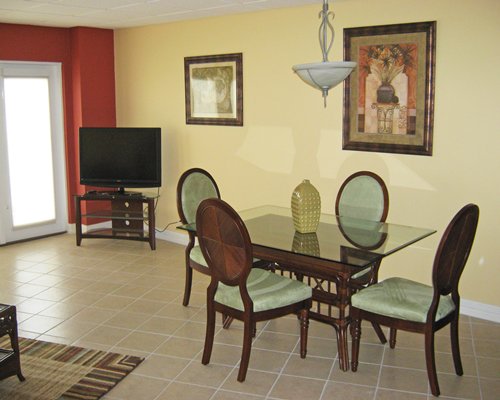 A well furnished dining room with a glass top table and television.