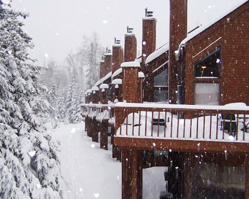 A balcony view of multi story resort units with pine trees covered in snow.