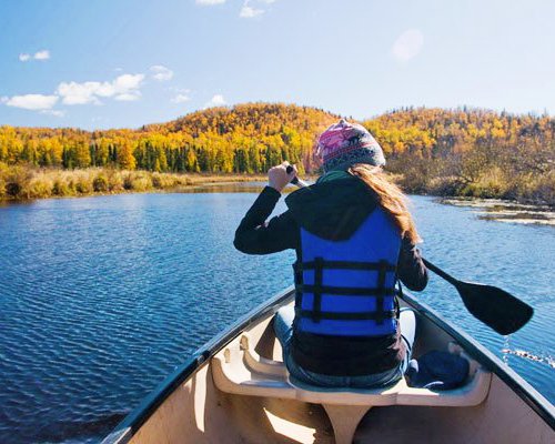 A woman canoeing at a lake surrounded by wooded area.