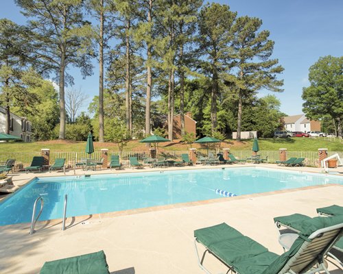 Outdoor swimming pool with chaise lounge chairs and sunshades alongside wooded area.