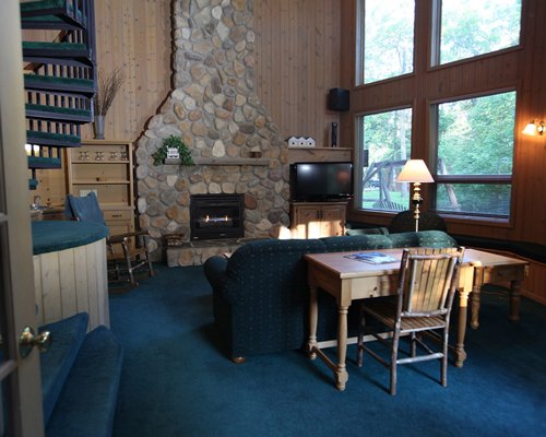 A well furnished living room with television dining area fire in the fireplace and spiral stairway.