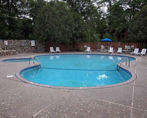 Outdoor swimming pool with chaise lounge chairs and sunshades surrounded by wooded area.