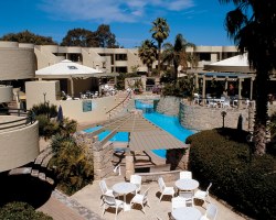 A BALCONY VIEW OF AN OUTDOOR POOL ALONGSIDE MULTI STORY RESORT UNITS.