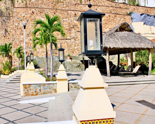 Pathway alongside a thatched sunshade with chaise lounge chairs.