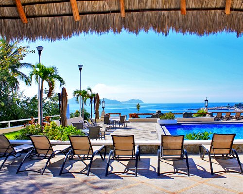 An outdoor swimming pool with chaise lounge chairs facing the ocean.