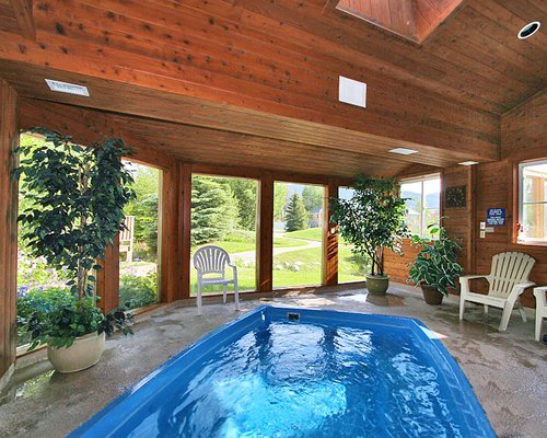 Indoor swimming pool with patio chairs and outside view.