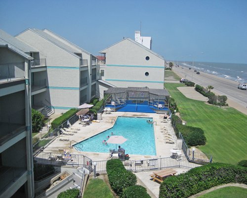 An aerial view of an outdoor swimming pool with chaise lounge chairs and sunshades alongside the waterfront.