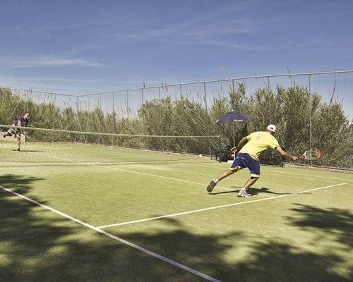 Two people playing in an outdoor tennis court surrounded by wooded area.