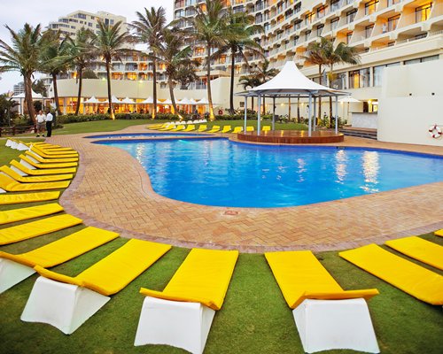 Outdoor swimming pool with chaise lounge chairs and sunshade alongside multiple unit balconies.