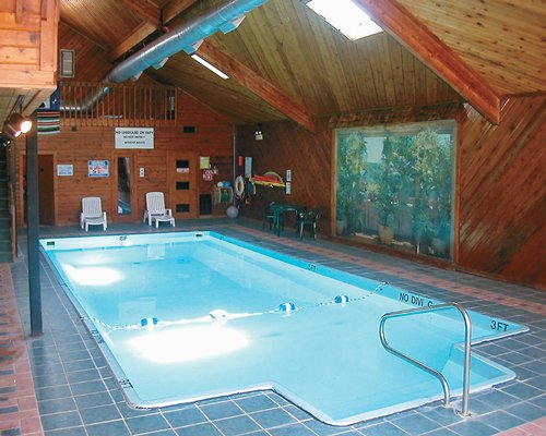 An indoor swimming pool with chaise lounge chairs and an outside view.