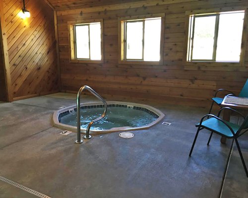 Indoor hot tub with patio chairs and outside view.