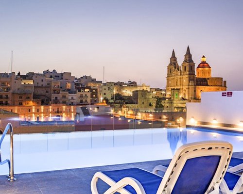 An outdoor swimming pool with chaise lounge chairs alongside the resort property at dusk.