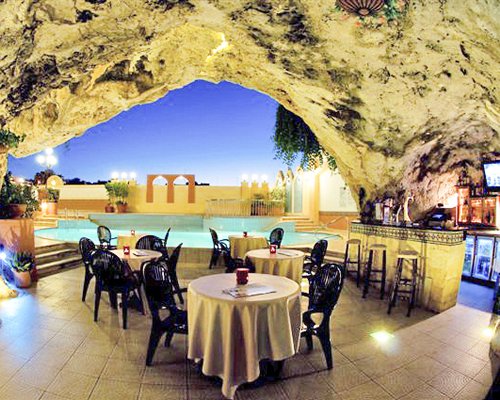 A well furnished indoor restaurant with a bar in a cave alongside a swimming pool.