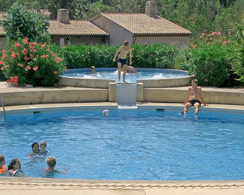 An outdoor swimming pool with a hot tub alongside resort units and landscaping.