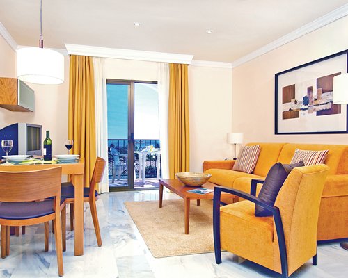 An open plan living and dining area with a television and balcony with patio furniture.