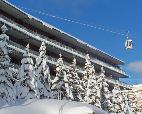 Exterior view of Palace Residence with pine trees and cable car during winter.