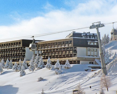 An exterior view of multi story units and pine trees covered in snow.