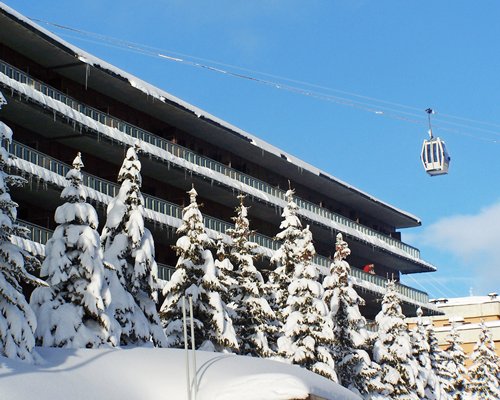 An exterior view of multi story resort units with pine trees covered in snow.