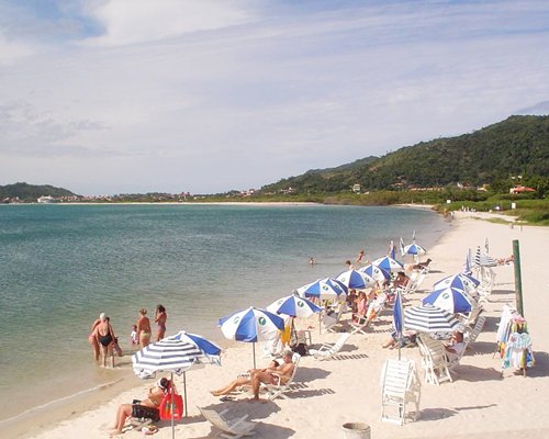 View of people at the beach with chaise lounge chairs and sunshades.