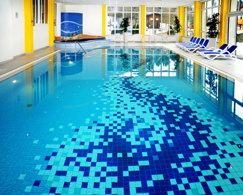An indoor swimming pool and hot tub with chaise lounge chairs.