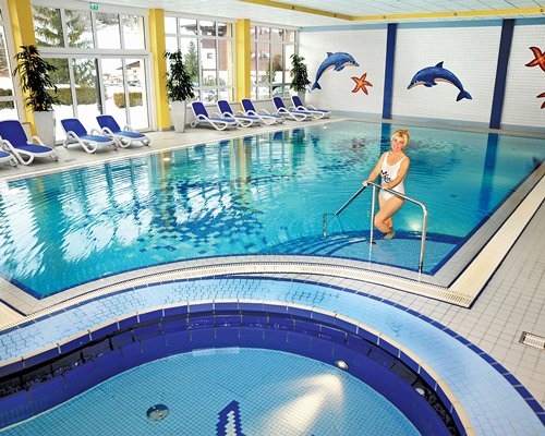 A women standing in the indoor swimming pool and hot tub with chaise lounge chairs.