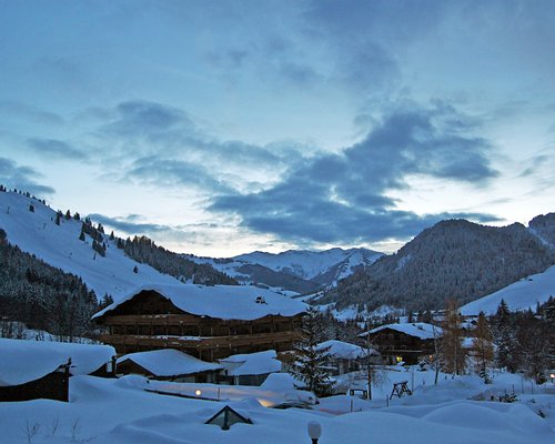 View of Marco Polo Club Alpina surrounded by wooded area alongside mountains during winter.