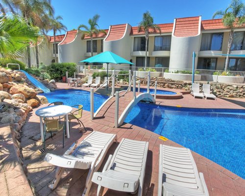 An outdoor swimming pool with chaise lounge chairs alongside multiple resort units.