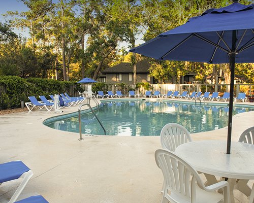 Outdoor swimming pool with patio chairs sunshades and chaise lounge chairs.