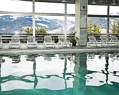 Indoor swimming pool with chaise lounge chairs and outside view.