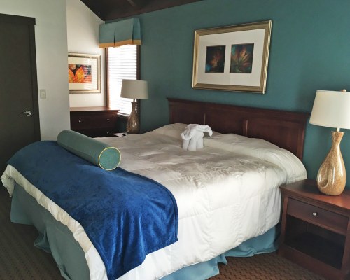 A WELL FURNISHED BEDROOM WITH A QUEEN BED AND LAMPSHADES.