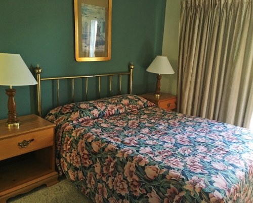 A WELL FURNISHED BEDROOM WITH A QUEEN BED LAMPSHADES AND AN OUTSIDE VIEW.