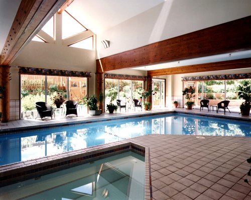 An indoor swimming pool with hot tub and patio furniture.