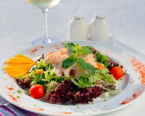 A salad on a plate with salt and pepper.
