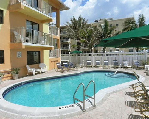 An outdoor swimming pool with chaise lounge chairs and patio furniture alongside multi story units.