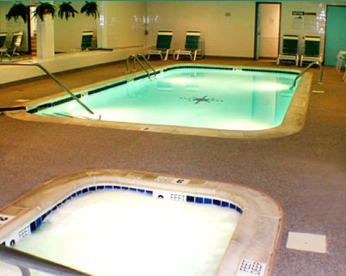 An indoor swimming pool and hot tub with chaise lounge chairs.