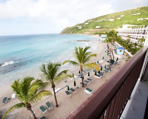 Balcony view of the beach with chaise lounge chairs sunshades and palm trees.