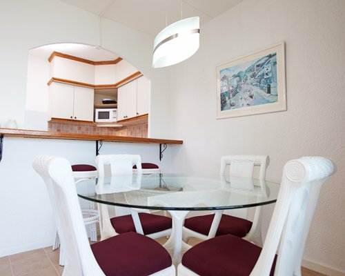 A well furnished glass topped dining table and a kitchen area with breakfast bar.