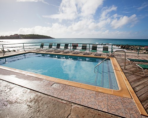 An outdoor swimming pool with chaise lounge chairs alongside the ocean.