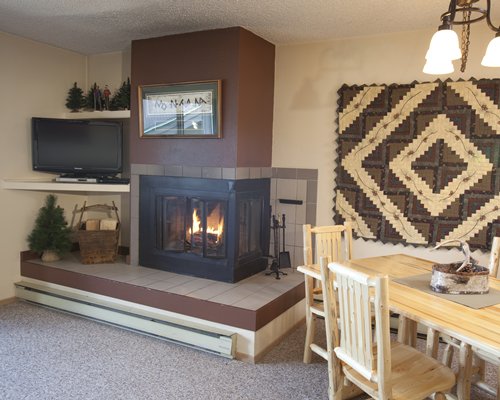 A well furnished living room with television fire in the fireplace and dining table.
